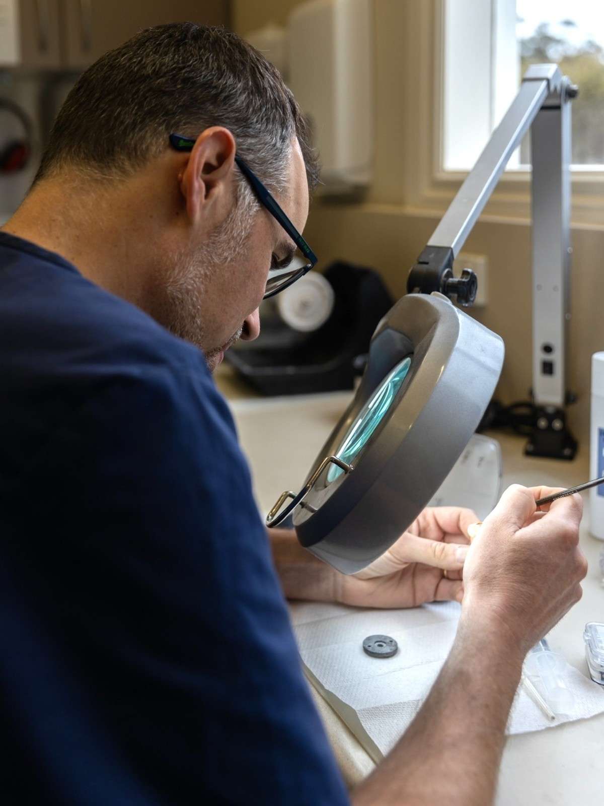 Dr. Andre Schertel uses a magnifying lamp and fine tools to work on a custom oral appliance.