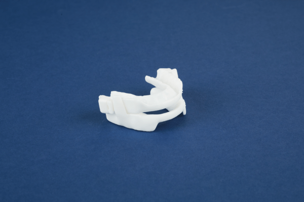 A white 3D-printed oral appliance for sleep therapy on a dark blue background.