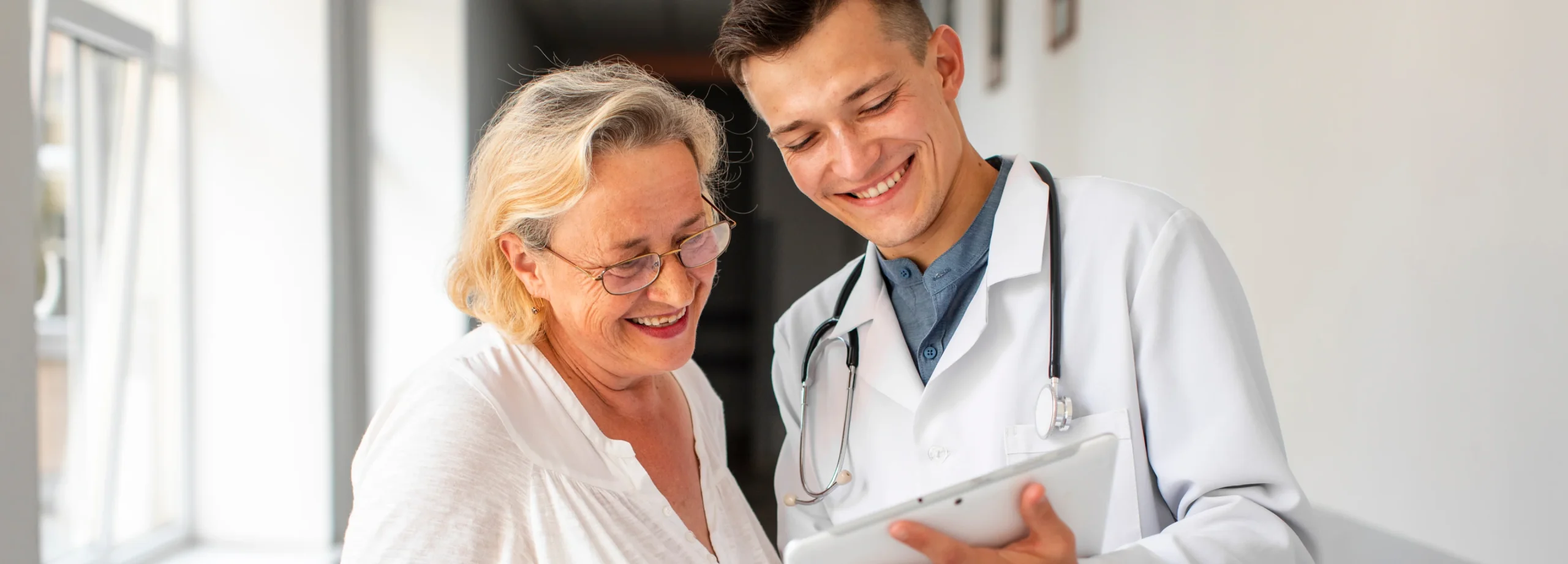 Male doctor with stethoscope showing tablet to smiling senior woman during consultation at sleep clinic